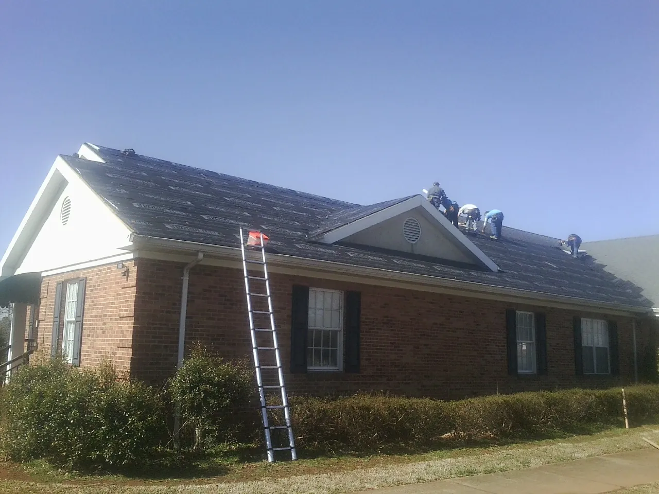 Crew tearing shingles off a brick ranch roof with a ladder set — Emergency Roof Repair work by our crew in Bear Mountain