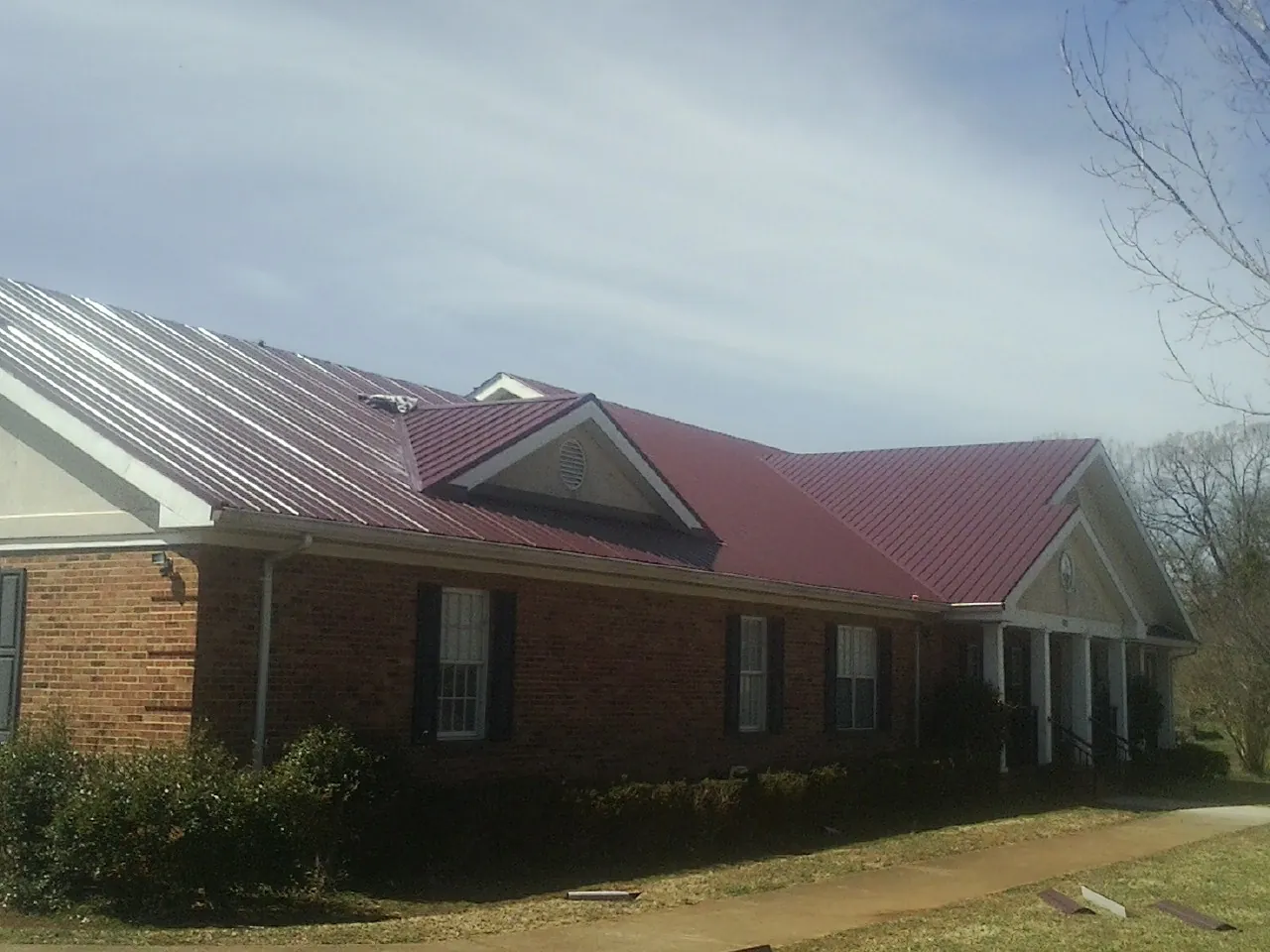 Red metal roof with gabled entries on a long brick building, from a Hail Damage Roof Repair job in Bear Mountain