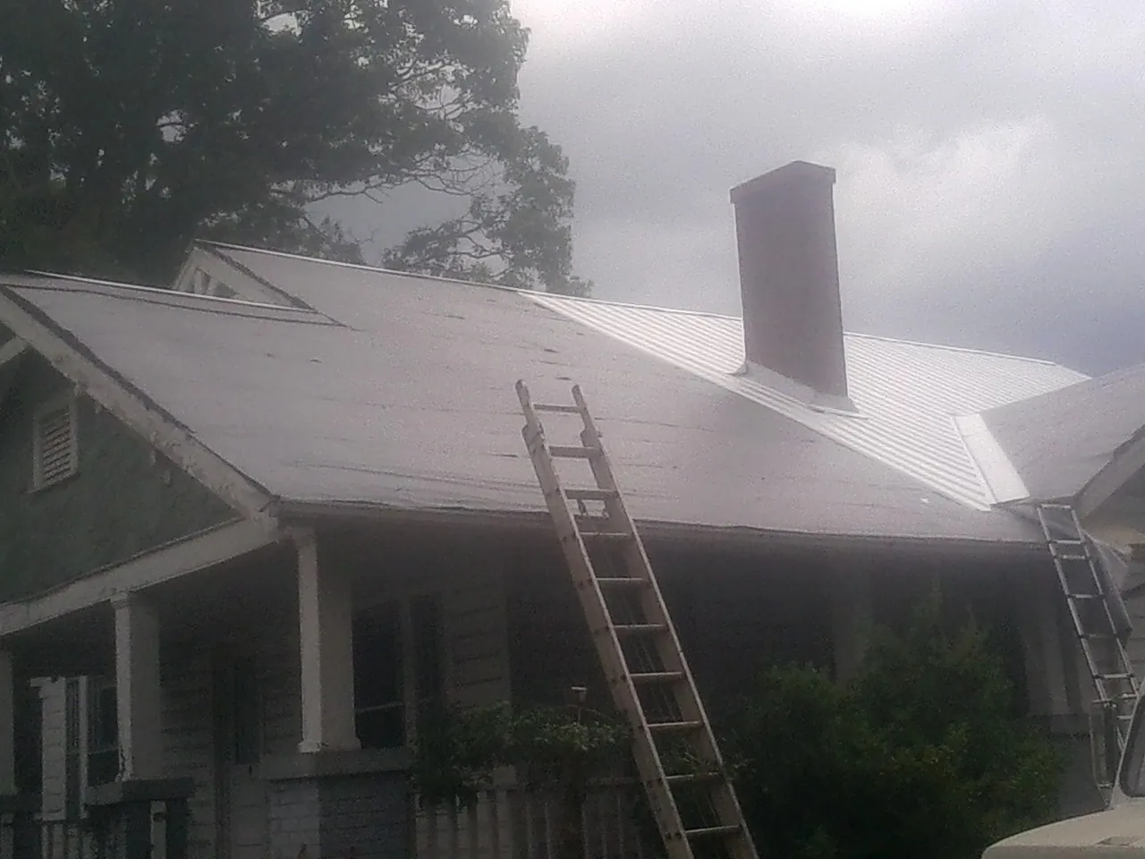 Ladders against a metal roof on an older home with a brick chimney in Bear Mountain