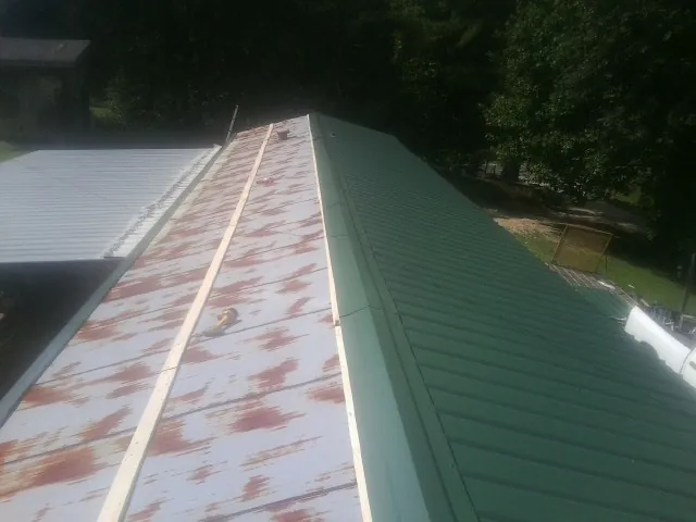 Old rusted panels beside newly installed green metal roofing — Wind Damage Roof Repair by Roofing Brothers in Bear Mountain