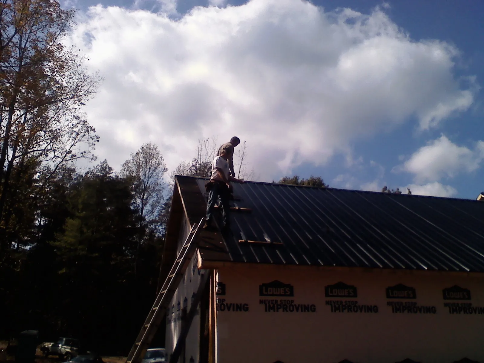 Roofer fastening dark metal panels high against a cloudy sky, from a Roof Inspection job in Bear Mountain
