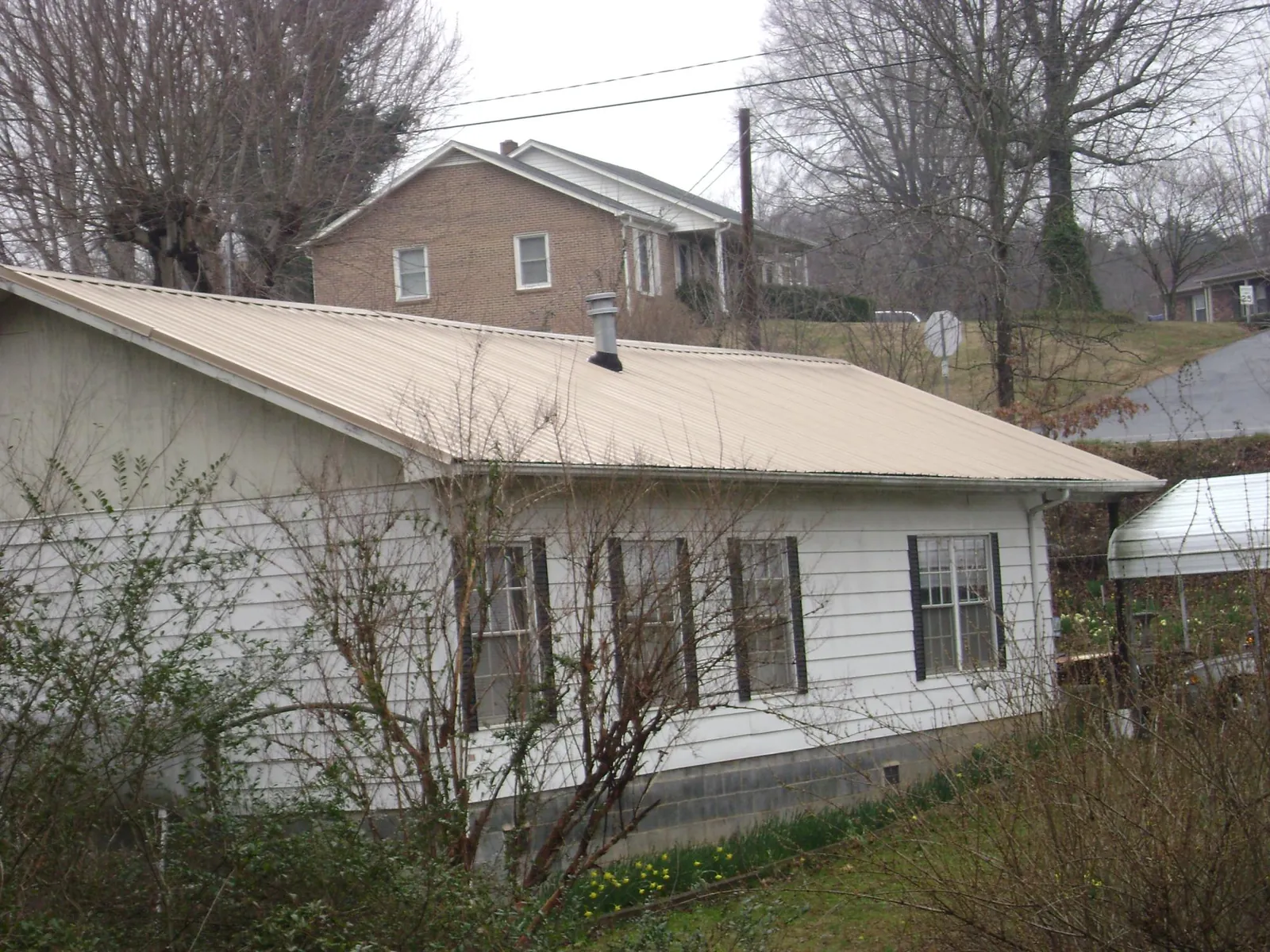 Tan metal roof on a white sided house set into a hillside — Commercial Roofing by Roofing Brothers in Bear Mountain